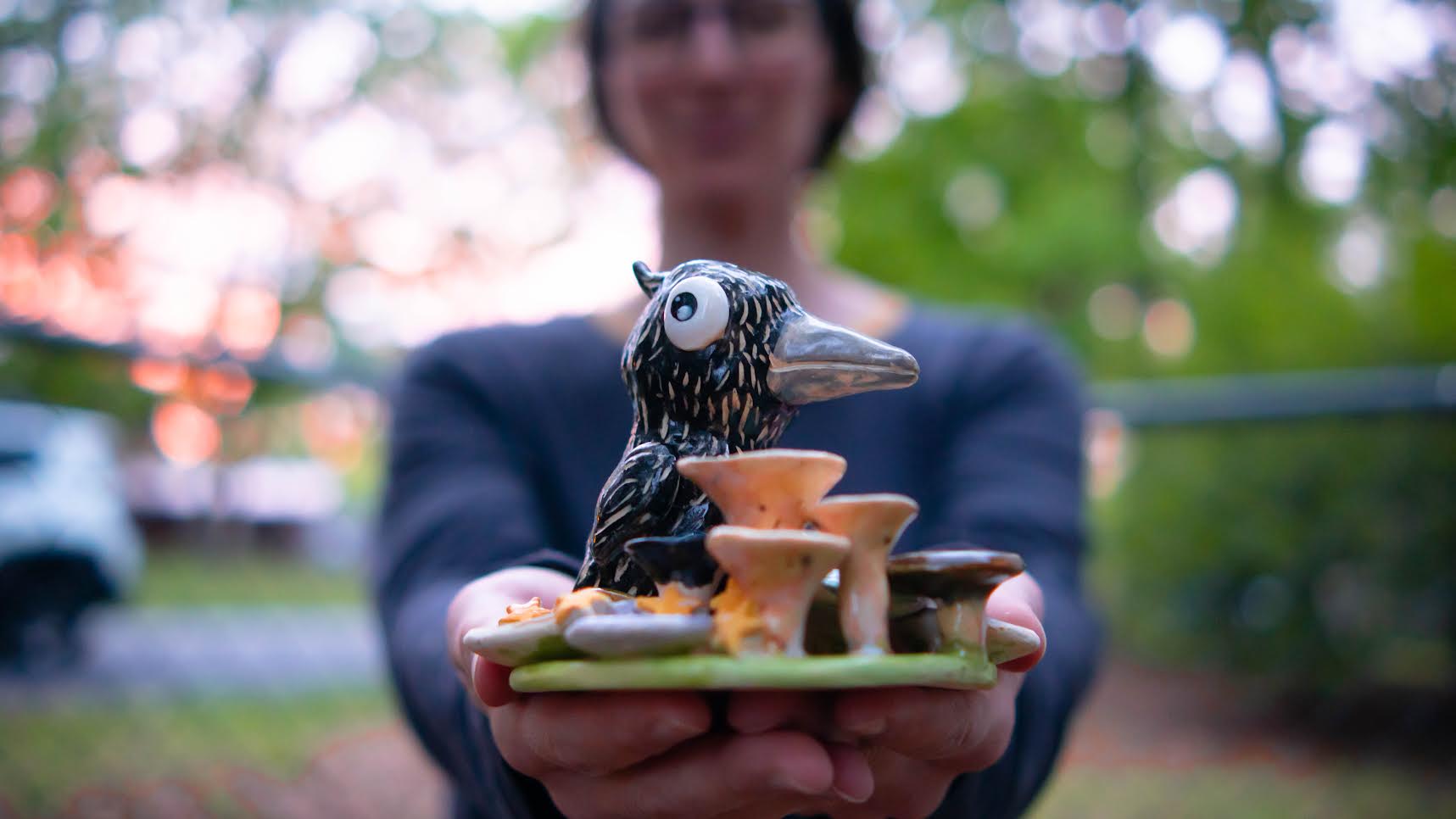 Small ceramic sculpture of a black bird among mushrooms, held in two hands