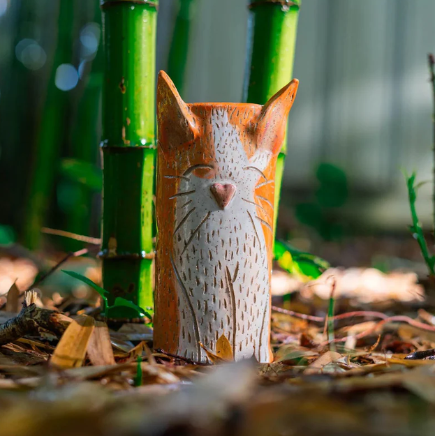 Hand-built ceramic cat vase with an orange face, standing among bamboo
